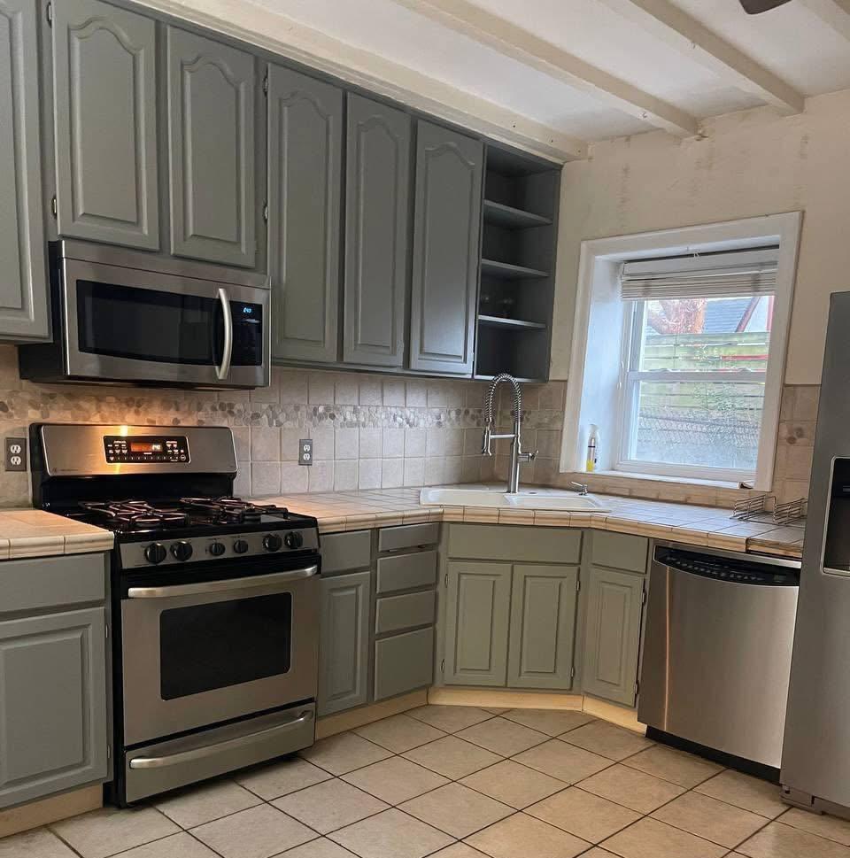 Sage-green kitchen with stainless appliances after cleaning